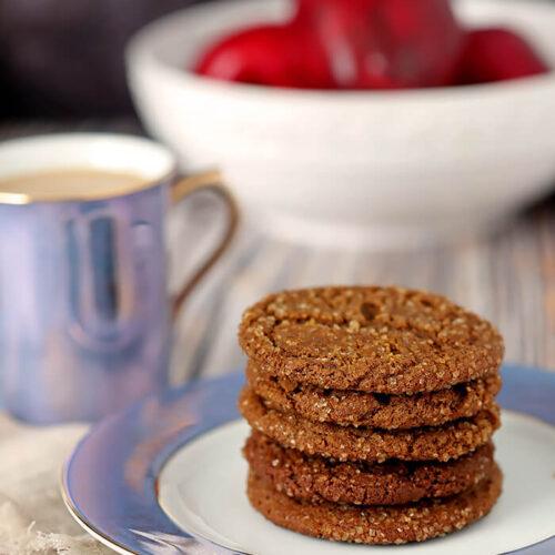 molasses cookies stacked on a plate with a cup of hot tea, steam rising