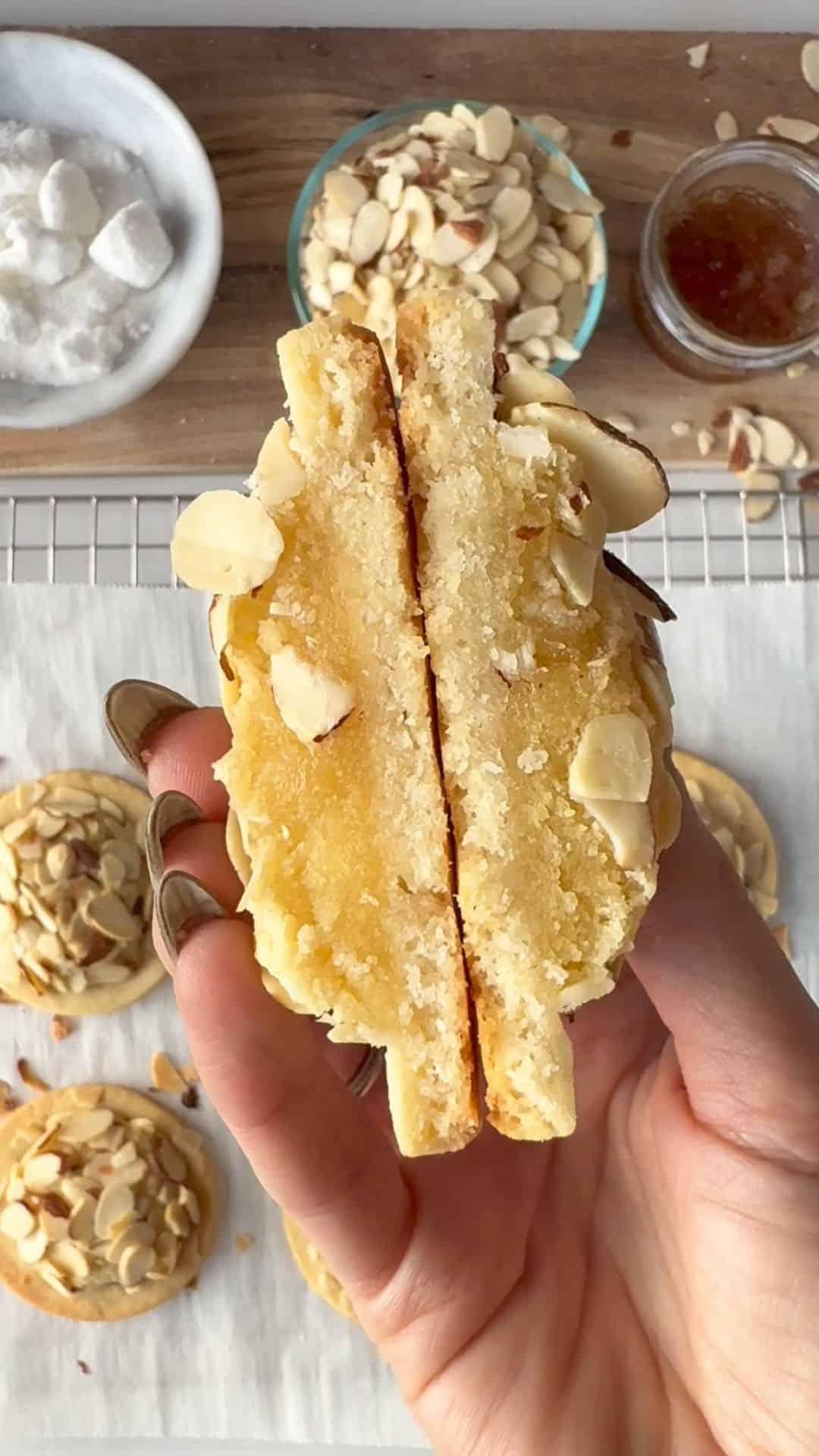 A person carefully piping glossy white icing onto an almond cookie to create a French tip effect