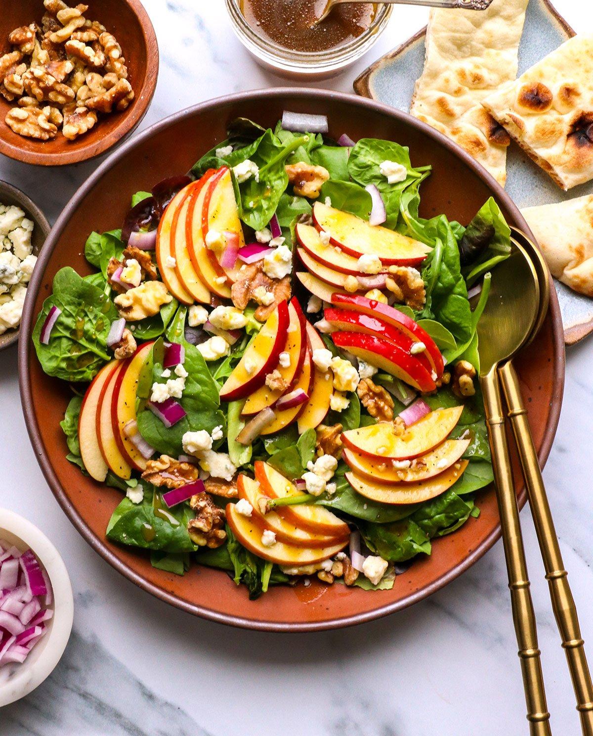 Hand drizzling honey over a colorful apple and walnut salad