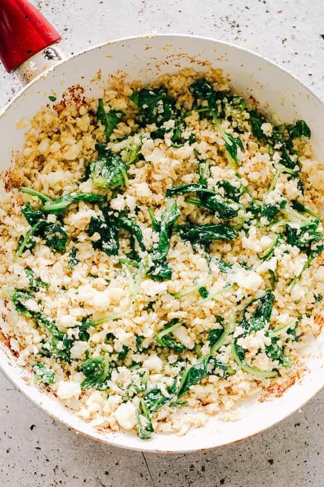 Cauliflower rice being sautéed in a pan with herbs and spices