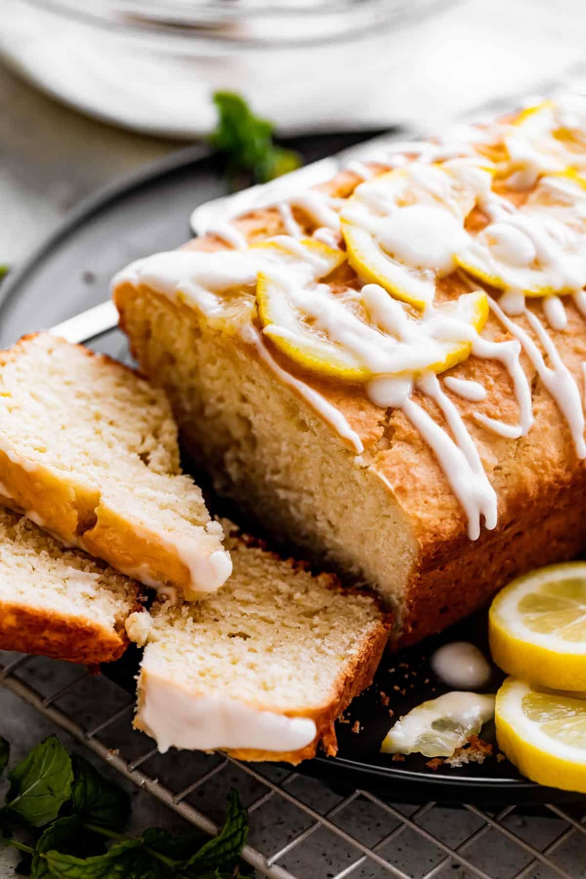 beautifully glazed lemon yogurt cake slice with a light, airy texture on a rustic wooden board, garnished with fresh lemon zest and mint
