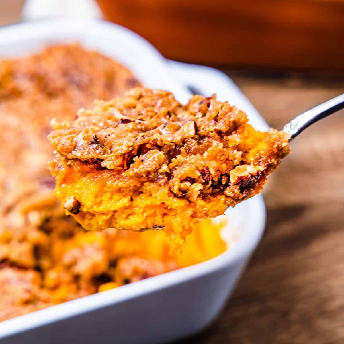 A spoon scooping a generous portion of sweet potato casserole, showing both the whipped potato and the crunchy topping