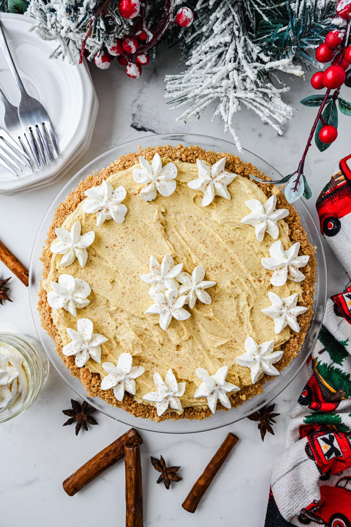Festive eggnog pie with a golden crust and fluffy nutmeg whipped cream topping on a rustic wooden table, holiday decorations in background