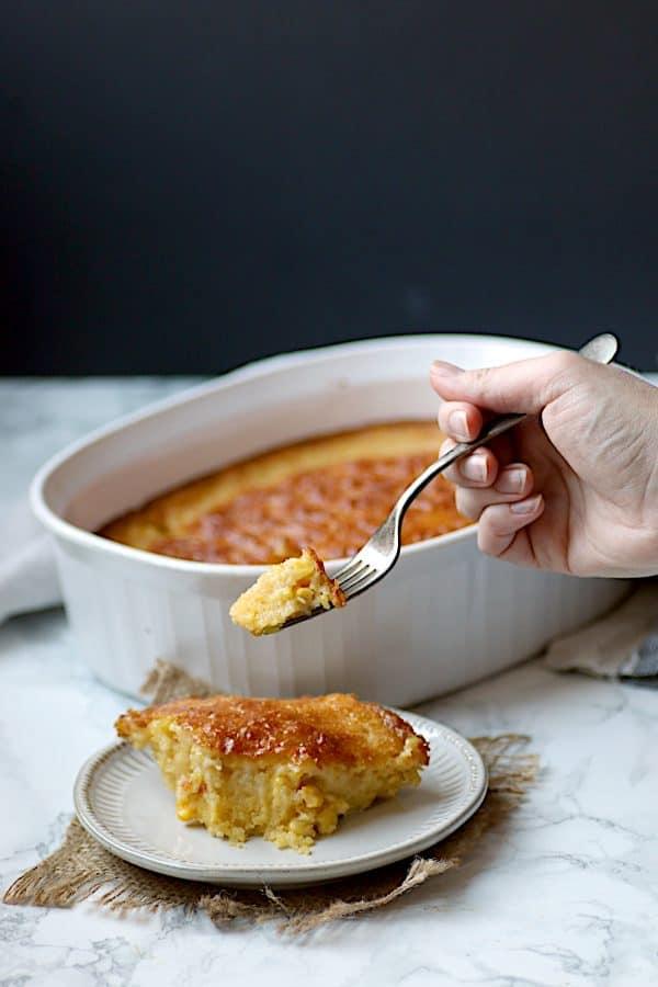 Hands serving a portion of corn casserole onto a plate