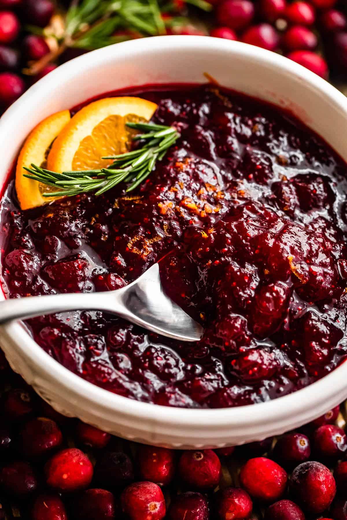 Homemade cranberry sauce in a decorative bowl with fresh cranberries and an orange slice, holiday setting