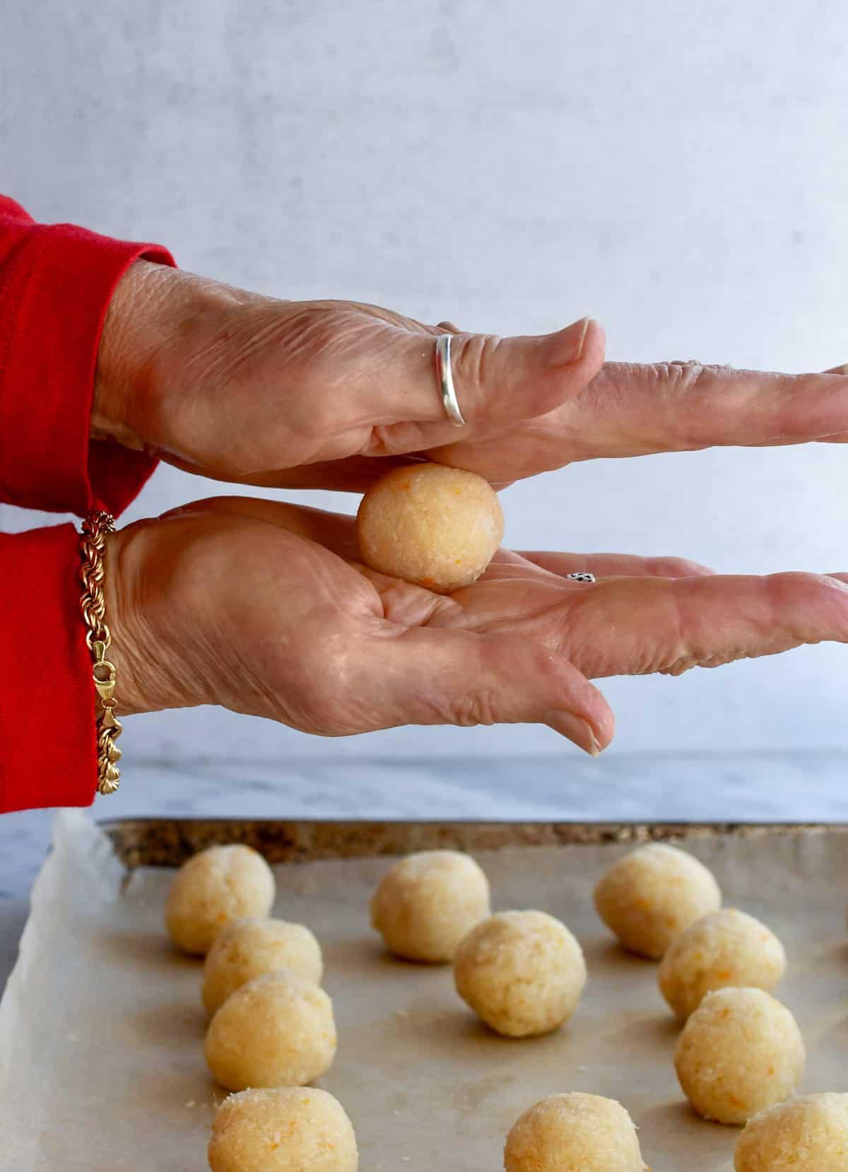 Close-up of freshly made coconut truffles being rolled in shredded coconut, hands visible