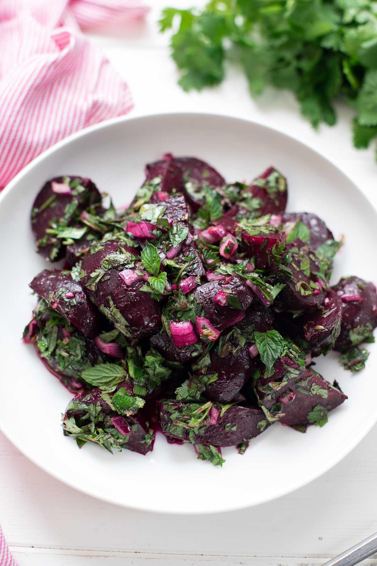 Hand tossing roasted beet salad with fresh herbs in a large bowl