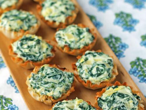 Spinach artichoke dip bites in mini phyllo cups on a party platter, close-up, golden brown, green specks, cheesy