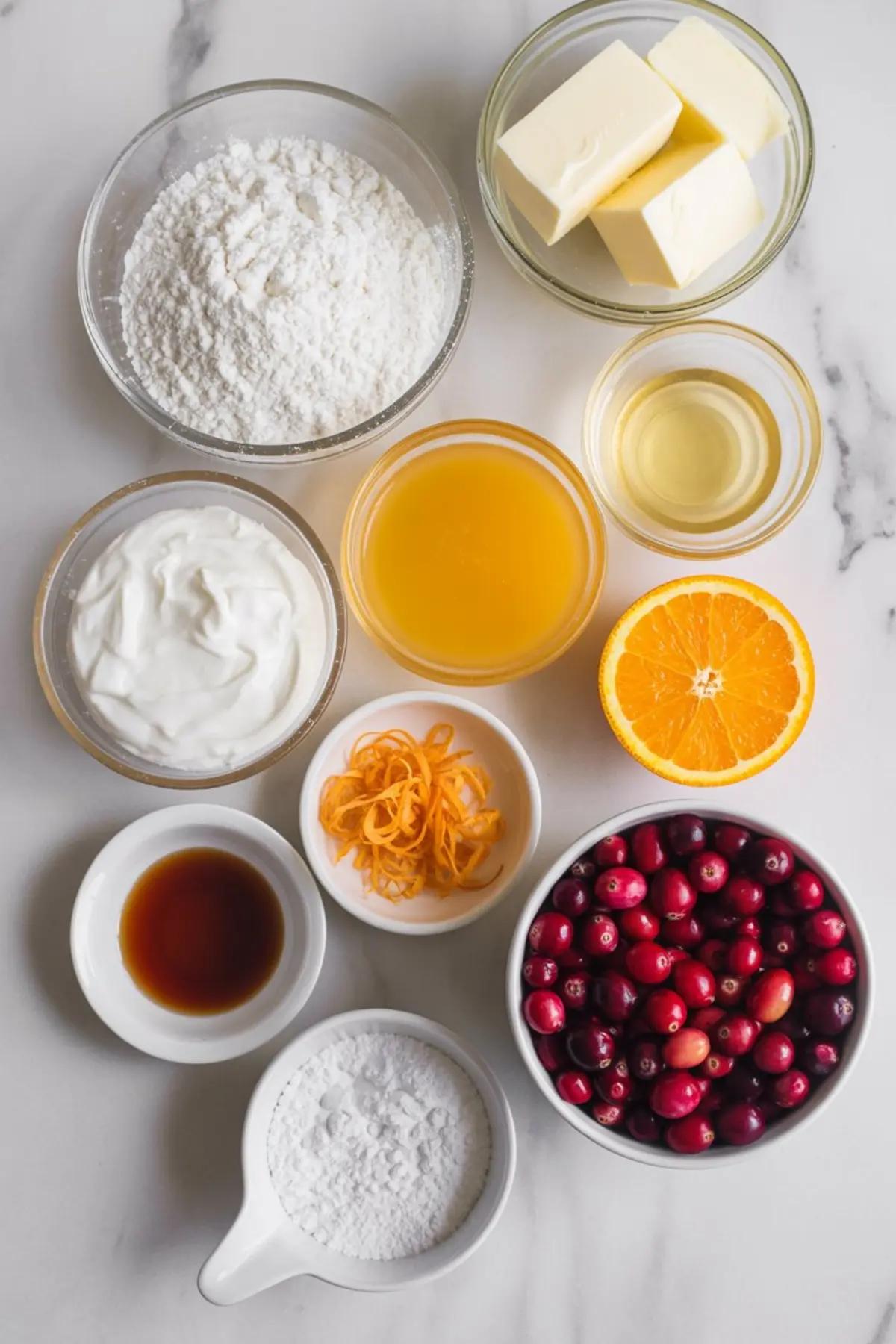 Ingredients for cranberry orange bread laid out on a kitchen counter: flour, sugar, eggs, butter, fresh cranberries, oranges.