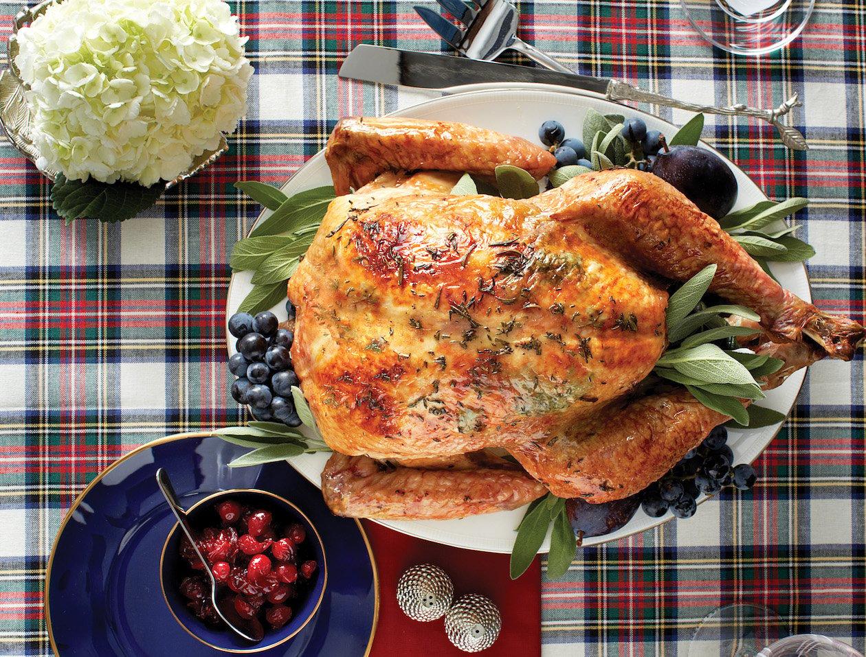 Chef happily presenting a perfectly roasted garlic herb turkey on a festive table, family in background