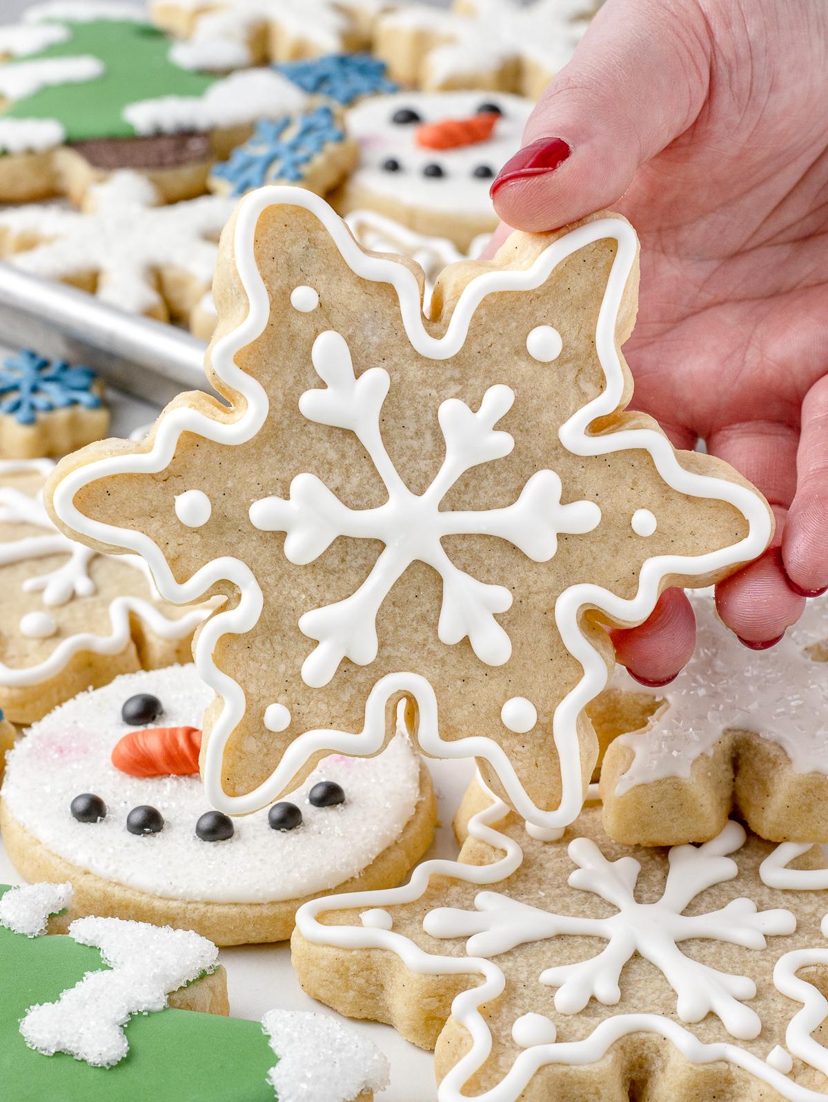 Hands decorating baked vanilla bean sugar cookies with simple white icing
