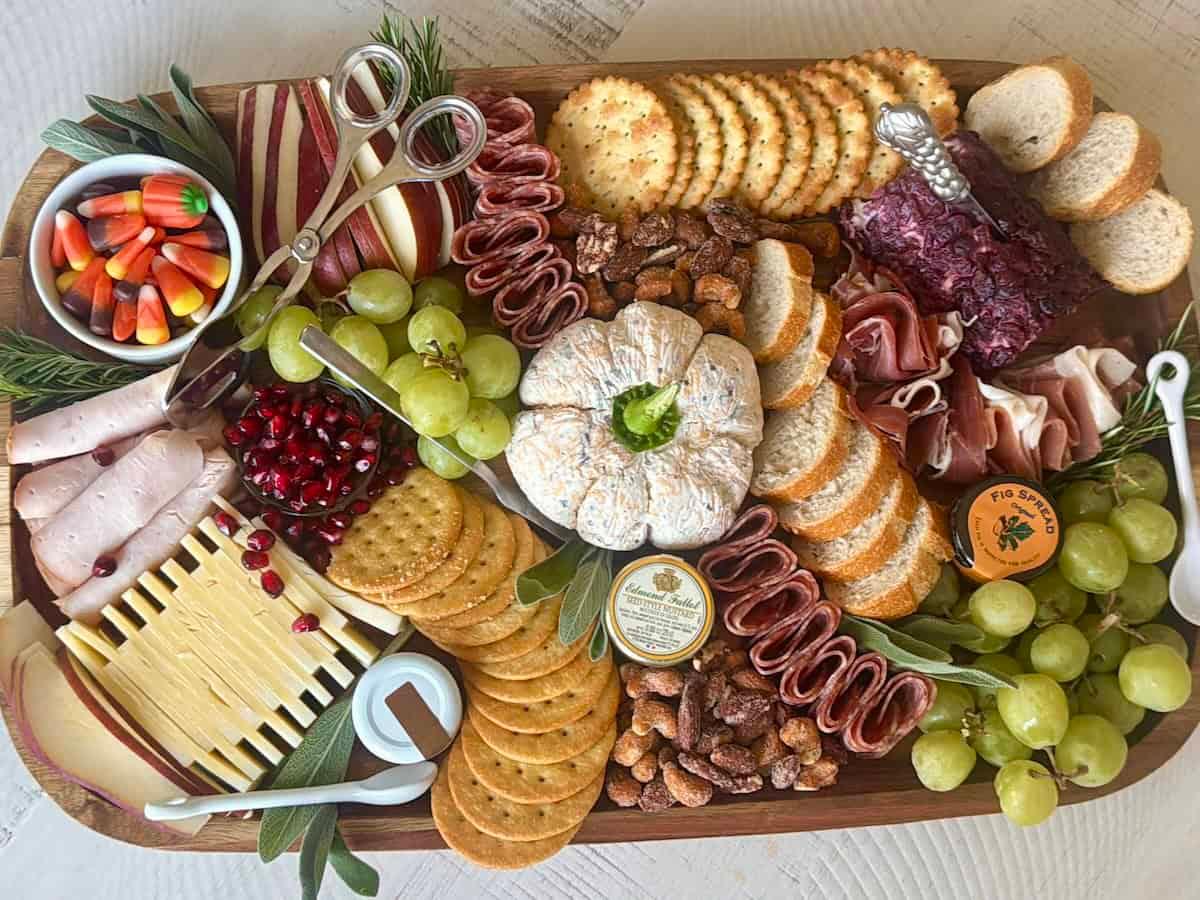 Beautifully presented herbed cheese ball on a charcuterie board with various crackers and grapes