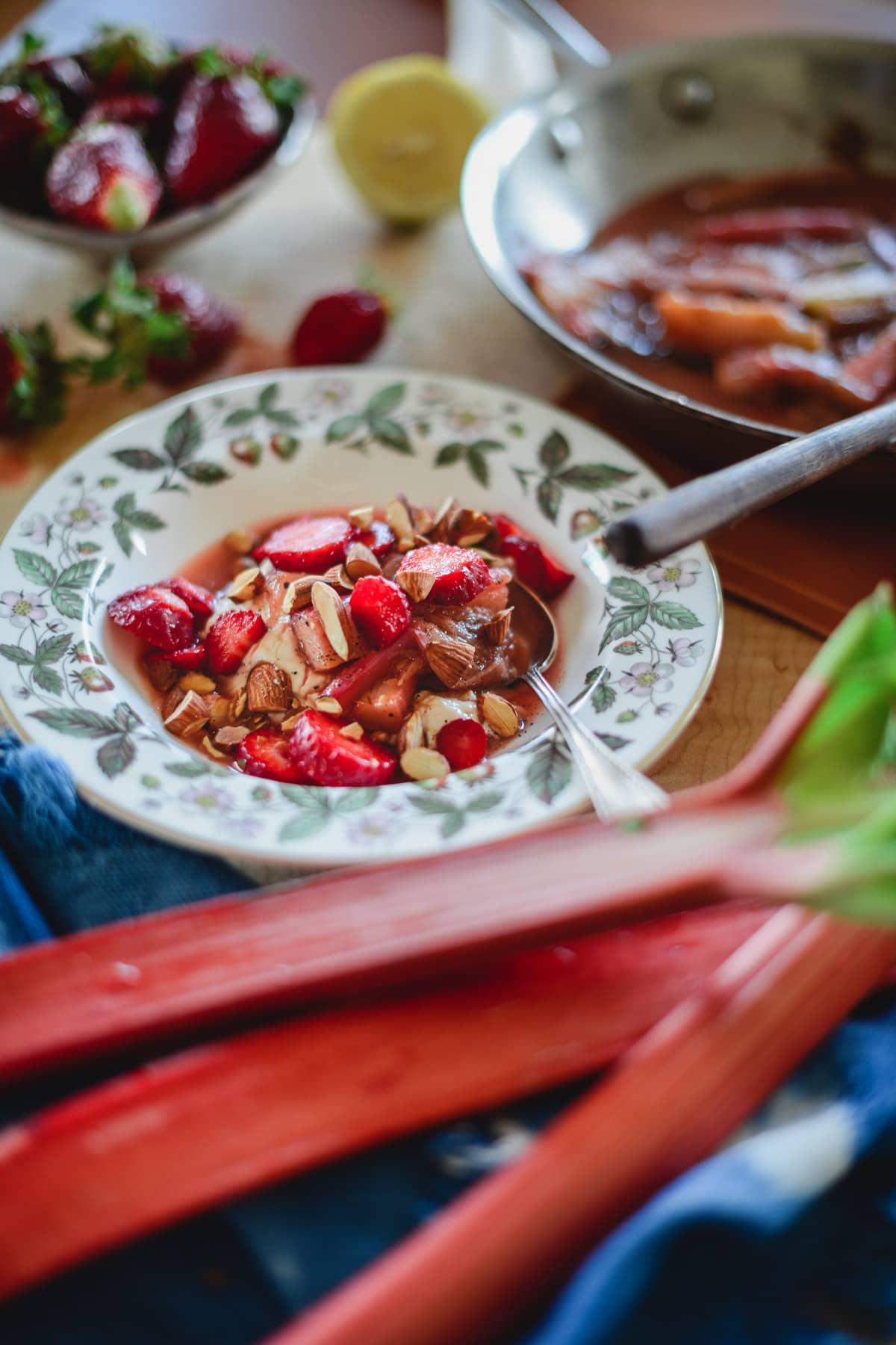 a bowl of bright red rhubarb pieces next to a stalk of fresh rhubarb