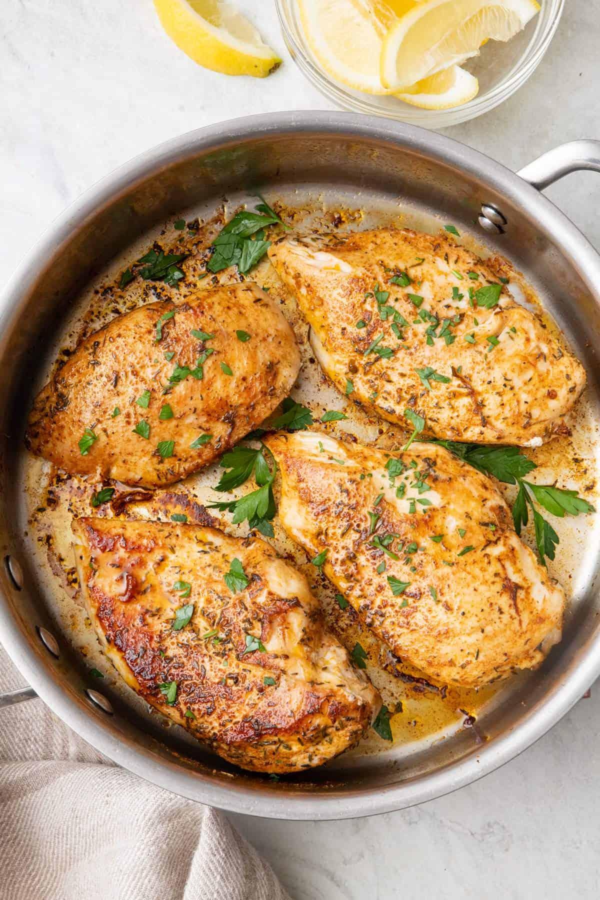 Close-up of golden brown pan-seared chicken breast in a skillet with melted butter and herbs, garnished with fresh parsley
