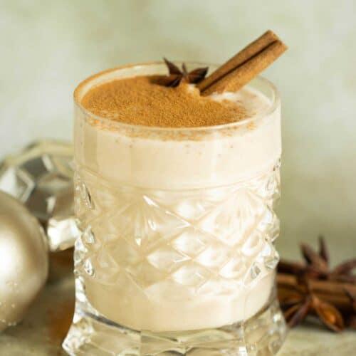 Authentic Puerto Rican Coquito in elegant glasses, festive holiday decor, warm lighting, cinnamon sticks and grated coconut garnish.
