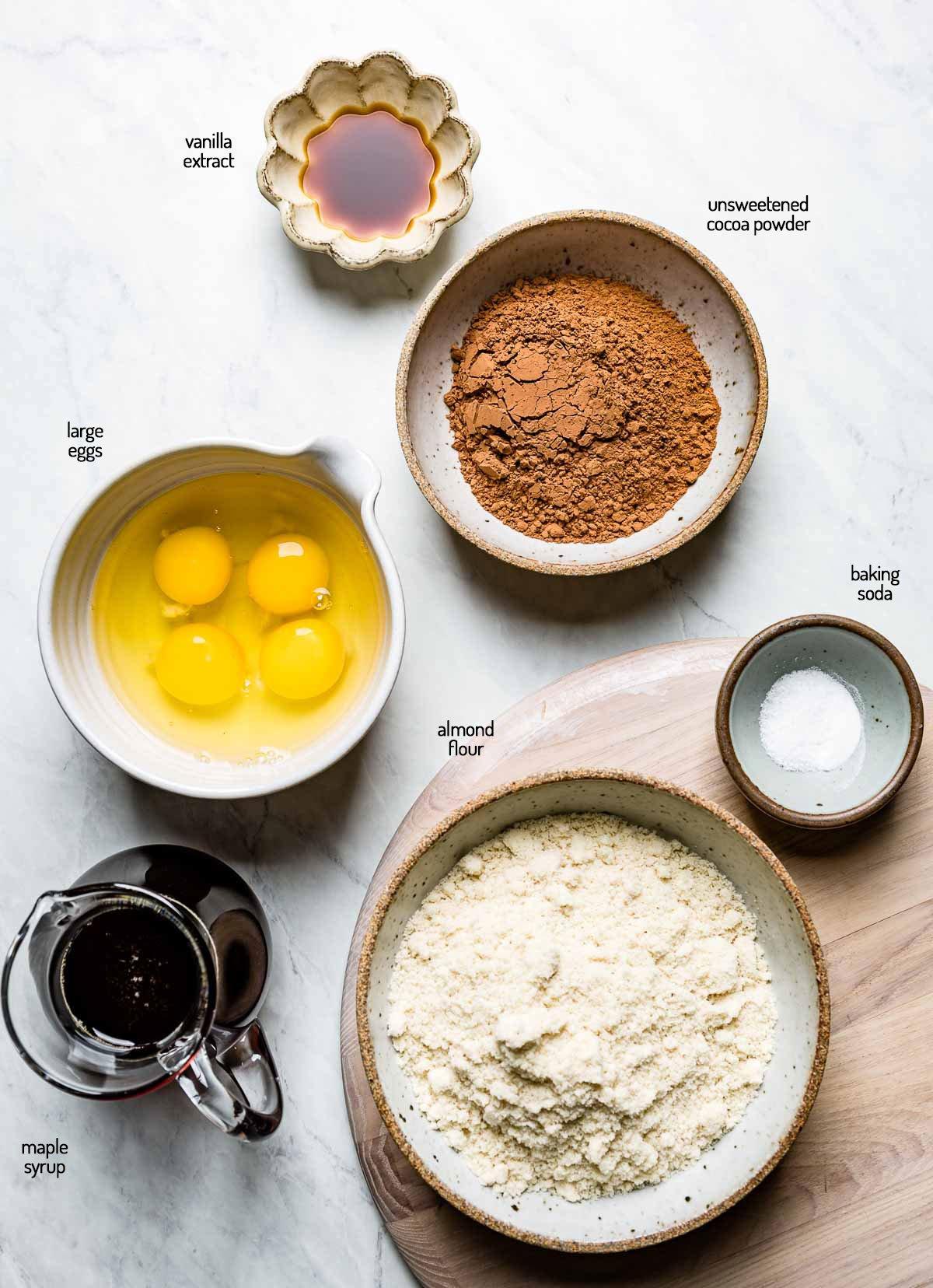 Ingredients for almond flour chocolate cake laid out on a kitchen counter: almond flour, cocoa powder, eggs, sugar, butter.
