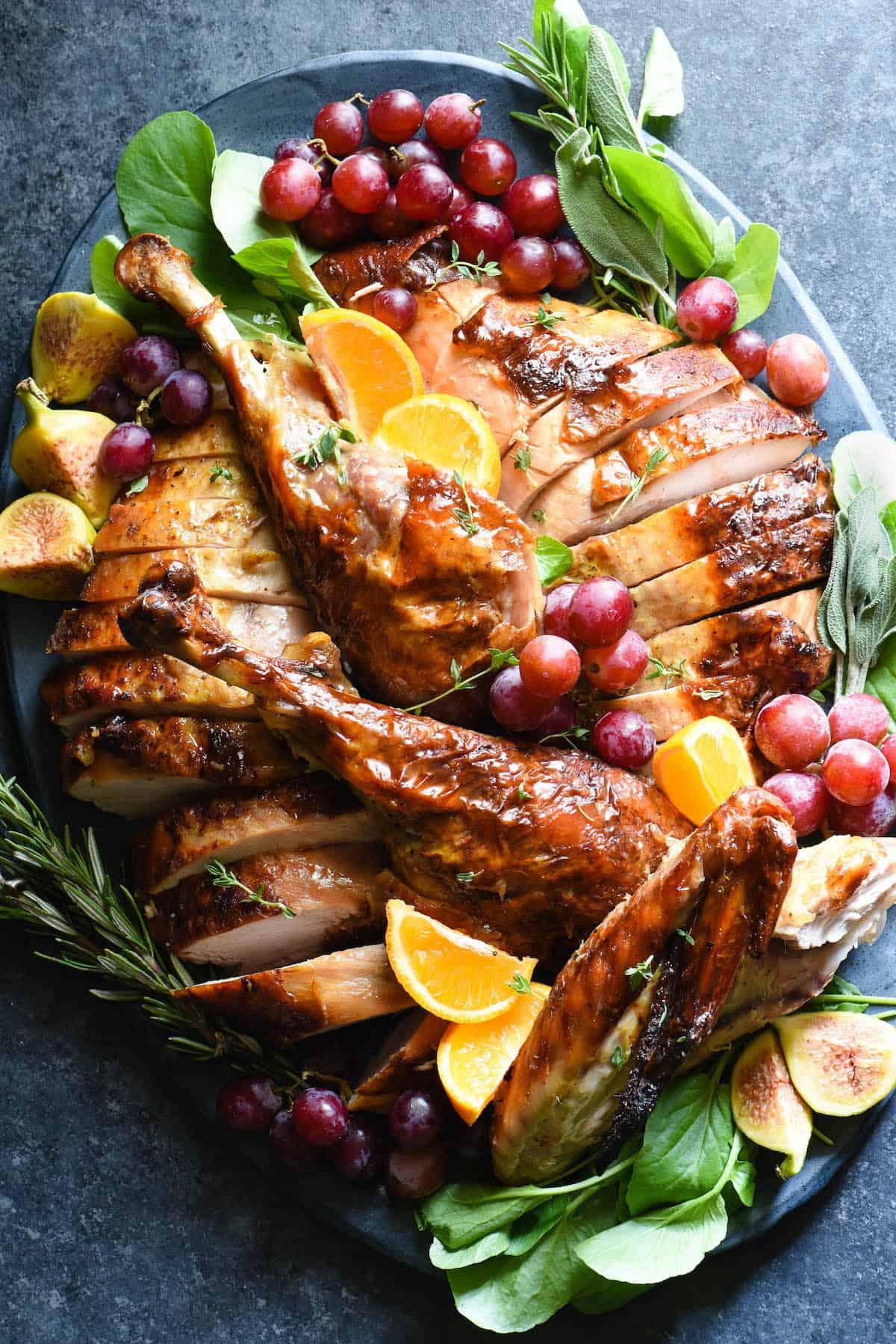 Vibrant, golden-brown maple glazed roast turkey with fresh orange slices, rosemary, and thyme on a festive platter, warm kitchen setting