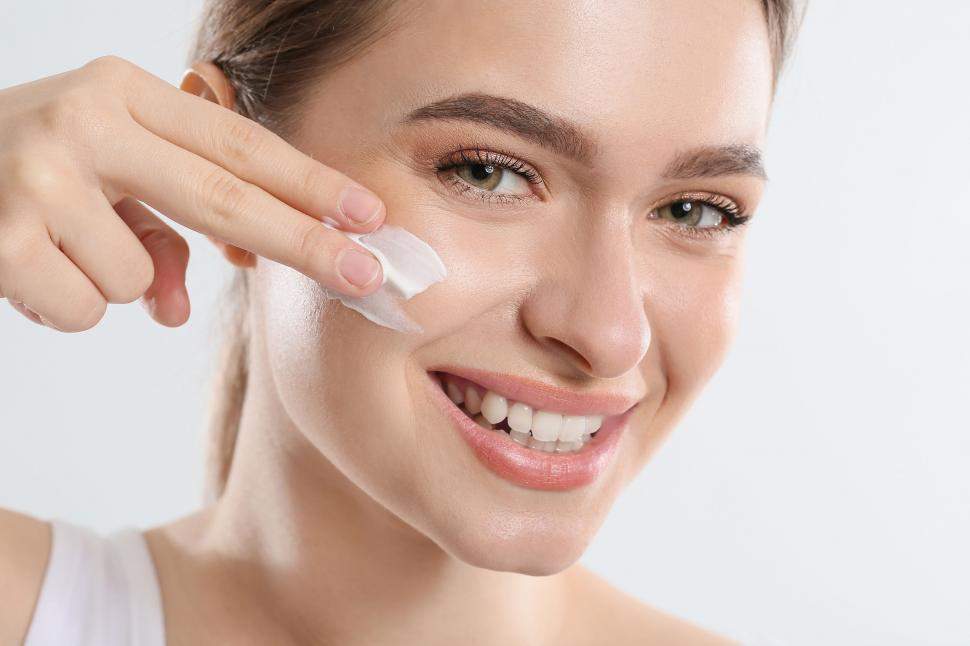 woman applying moisturizer to her face with a smile