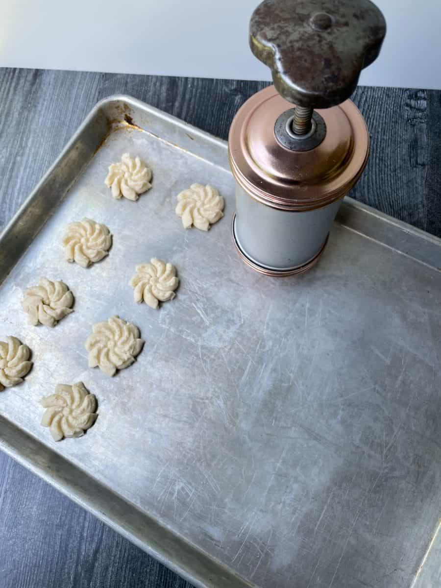 A close-up of raw spritz cookie dough being pressed onto a parchment-lined baking sheet