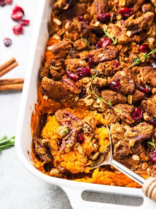 Vibrant roasted sweet potato casserole with a glistening, golden pecan-oat crust, steam rising slightly, in a ceramic baking dish on a rustic wooden table, surrounded by autumnal decorations and a cozy plaid napkin.