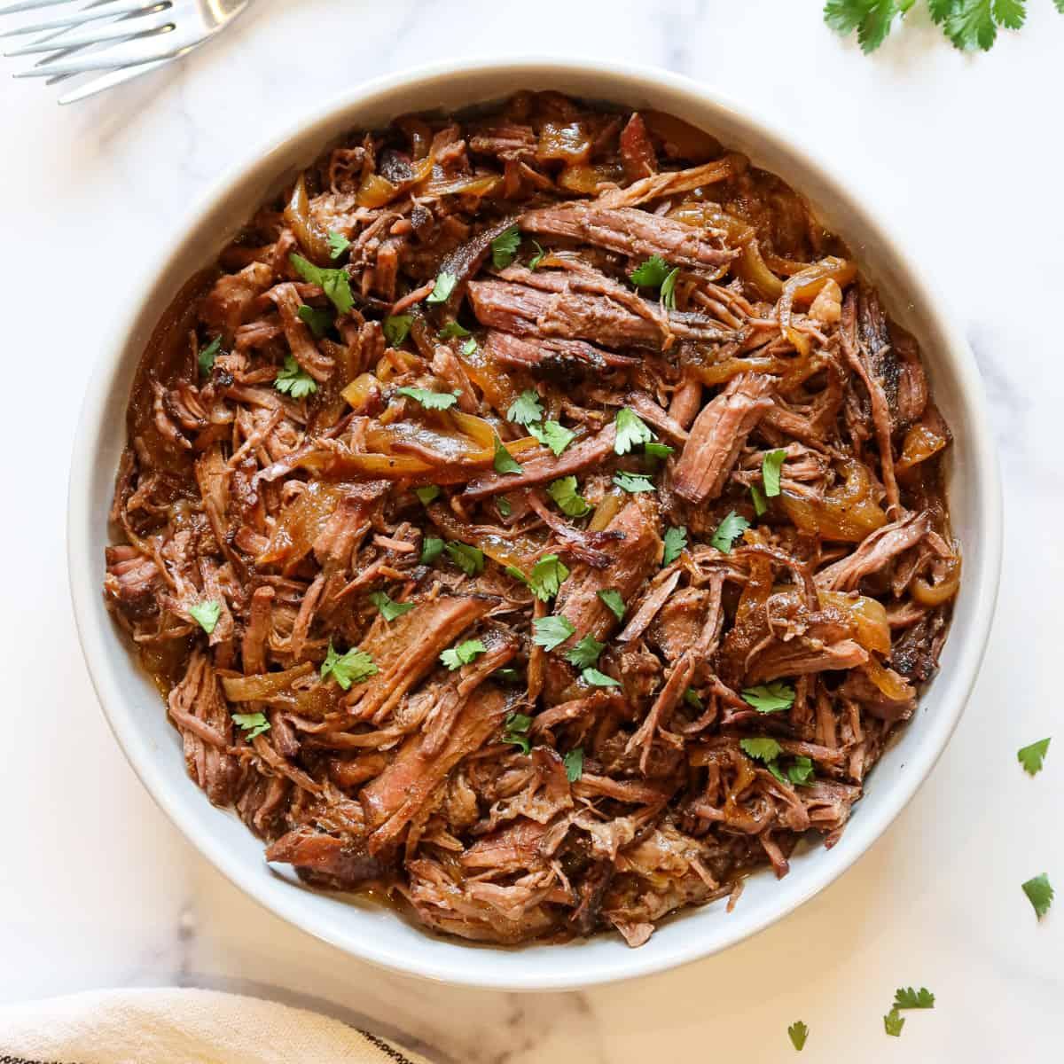 slow-cooked beef roast shredded with two forks, showing its tenderness