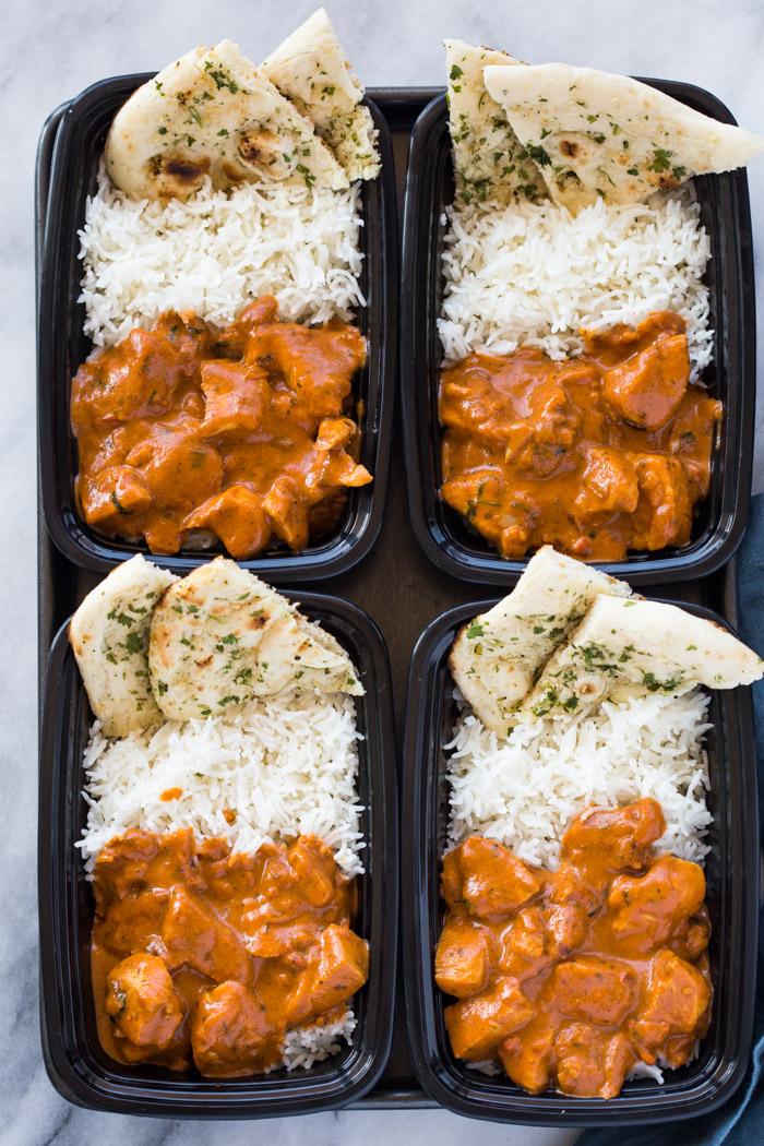 a complete meal setup with butter chicken, naan bread, rice, and side dishes