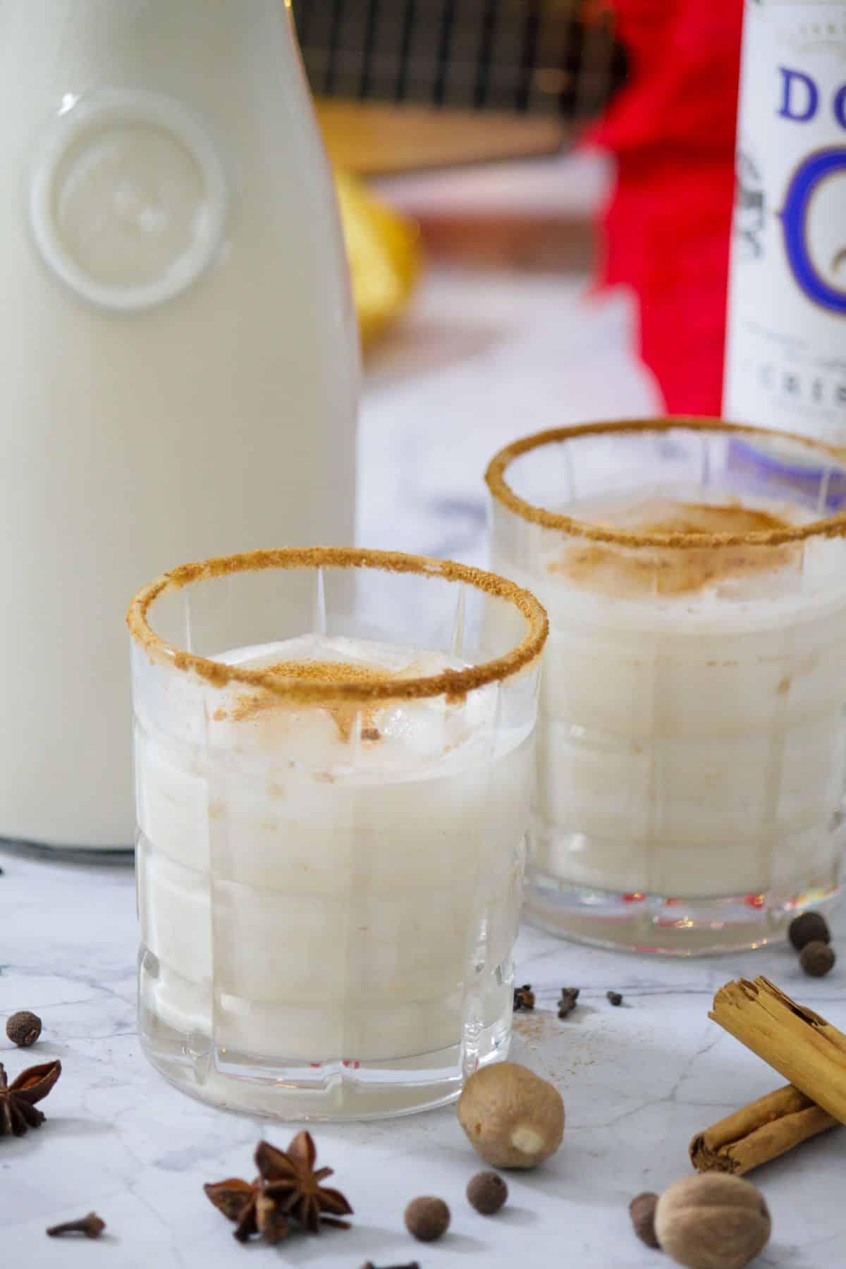 Festive Coquito bar setup with decorated glasses, cinnamon sticks, toasted coconut flakes, and bottle of rum