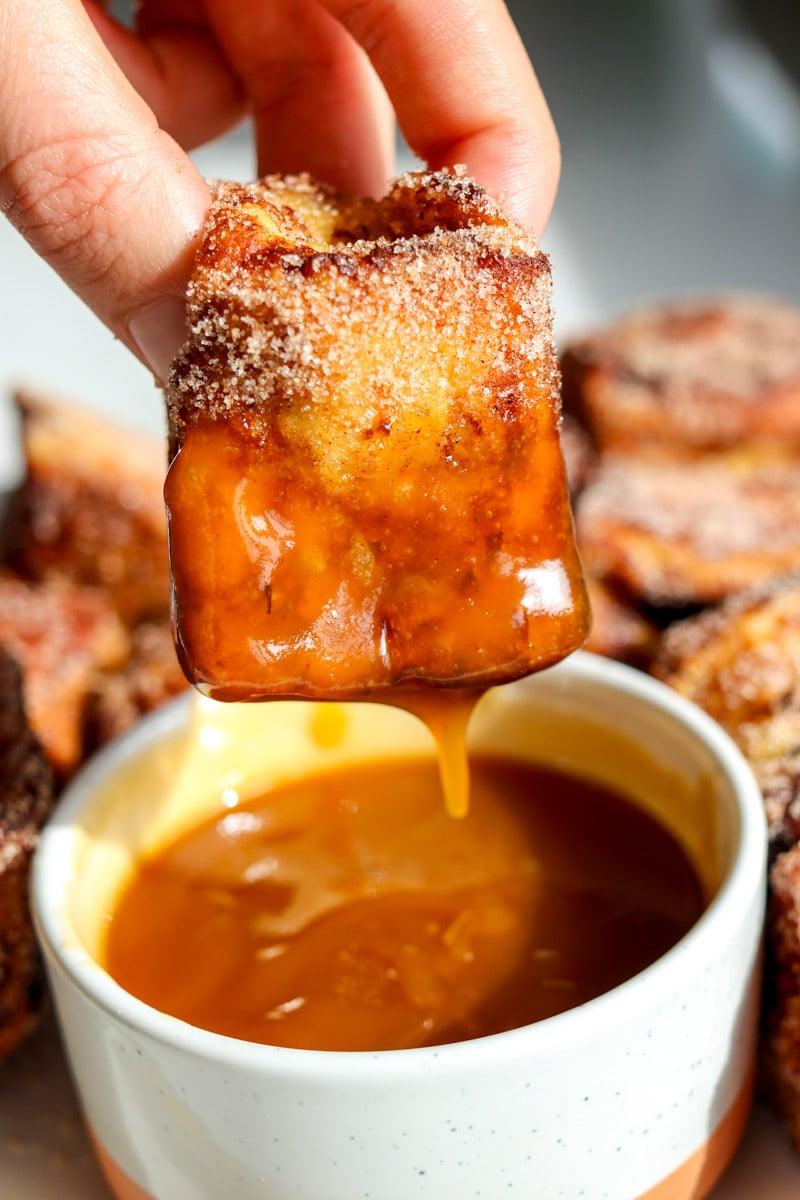 Hands dipping a cinnamon roll into French toast batter