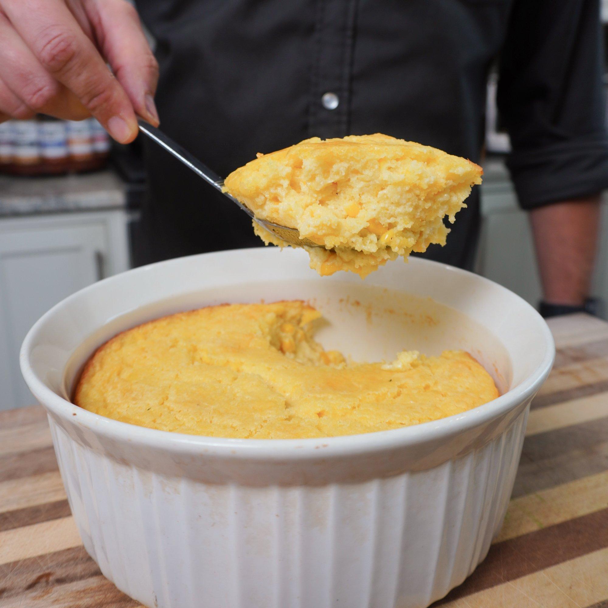 Someone scooping a generous portion of corn casserole onto a plate, showing the creamy texture inside
