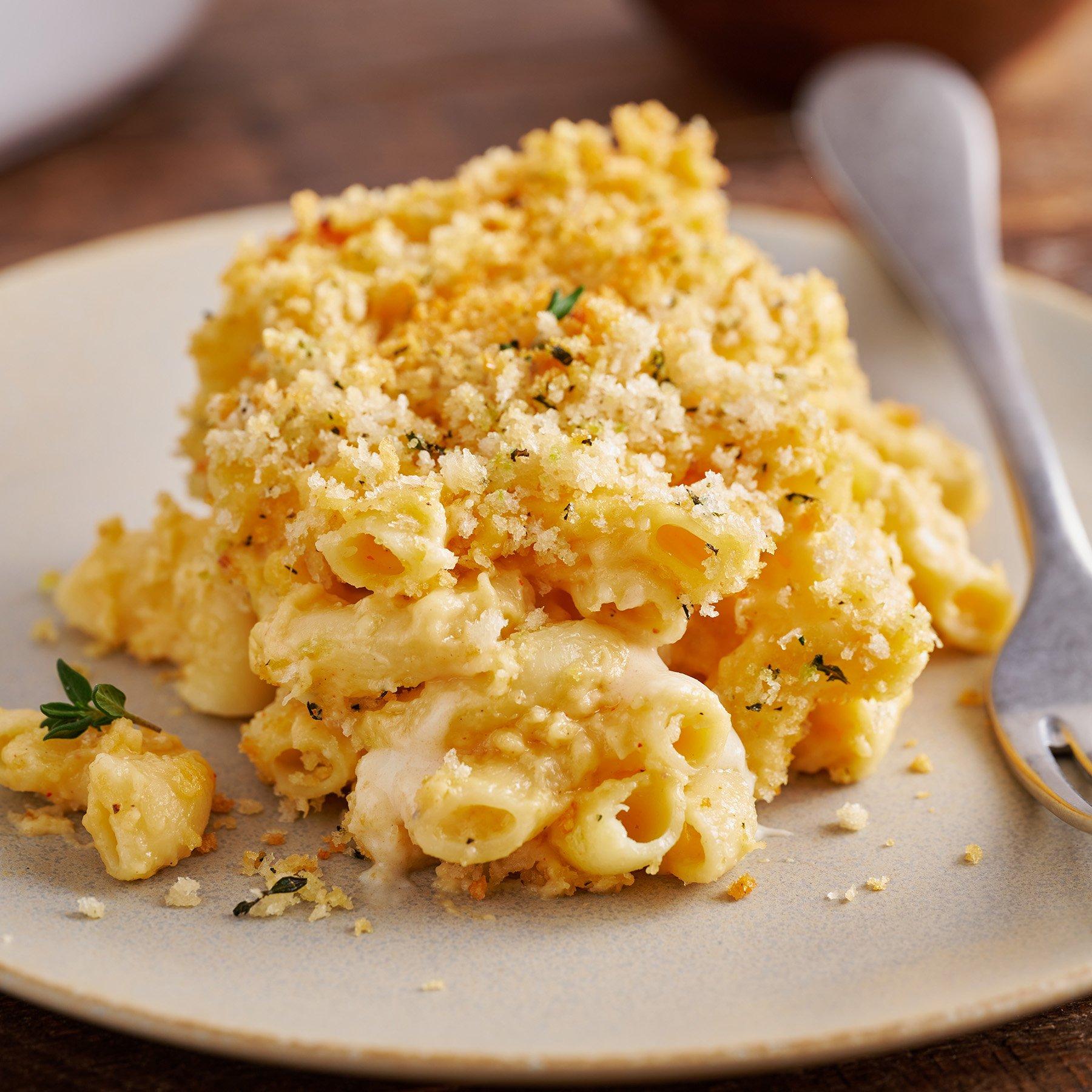 A hand dipping mac and cheese patty into panko breadcrumbs