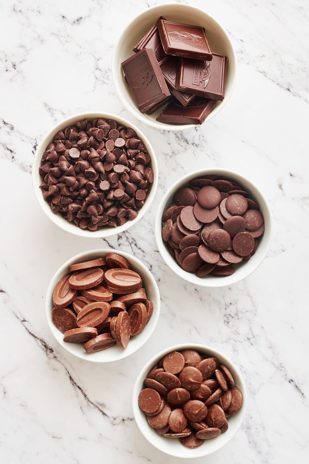 various types of chocolate chips and chunks in small bowls, ready for baking