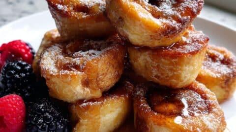 Close-up of cinnamon roll French toast bites stacked on a plate with glaze dripping