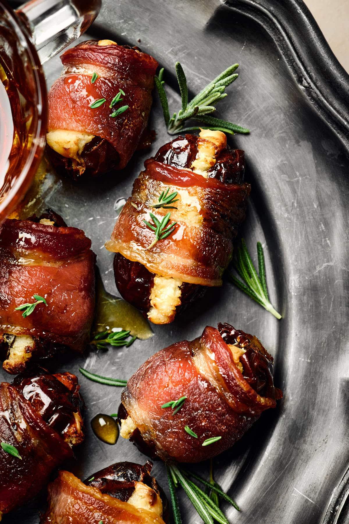 Overhead shot of a platter of bacon-wrapped dates with toothpicks, garnished with fresh herbs, ready to serve
