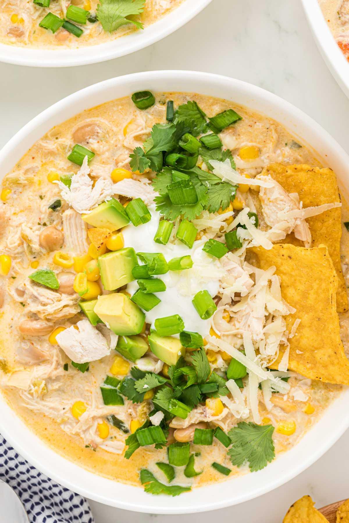 Serving suggestion of white chicken chili topped with avocado, cilantro, and sour cream, alongside cornbread