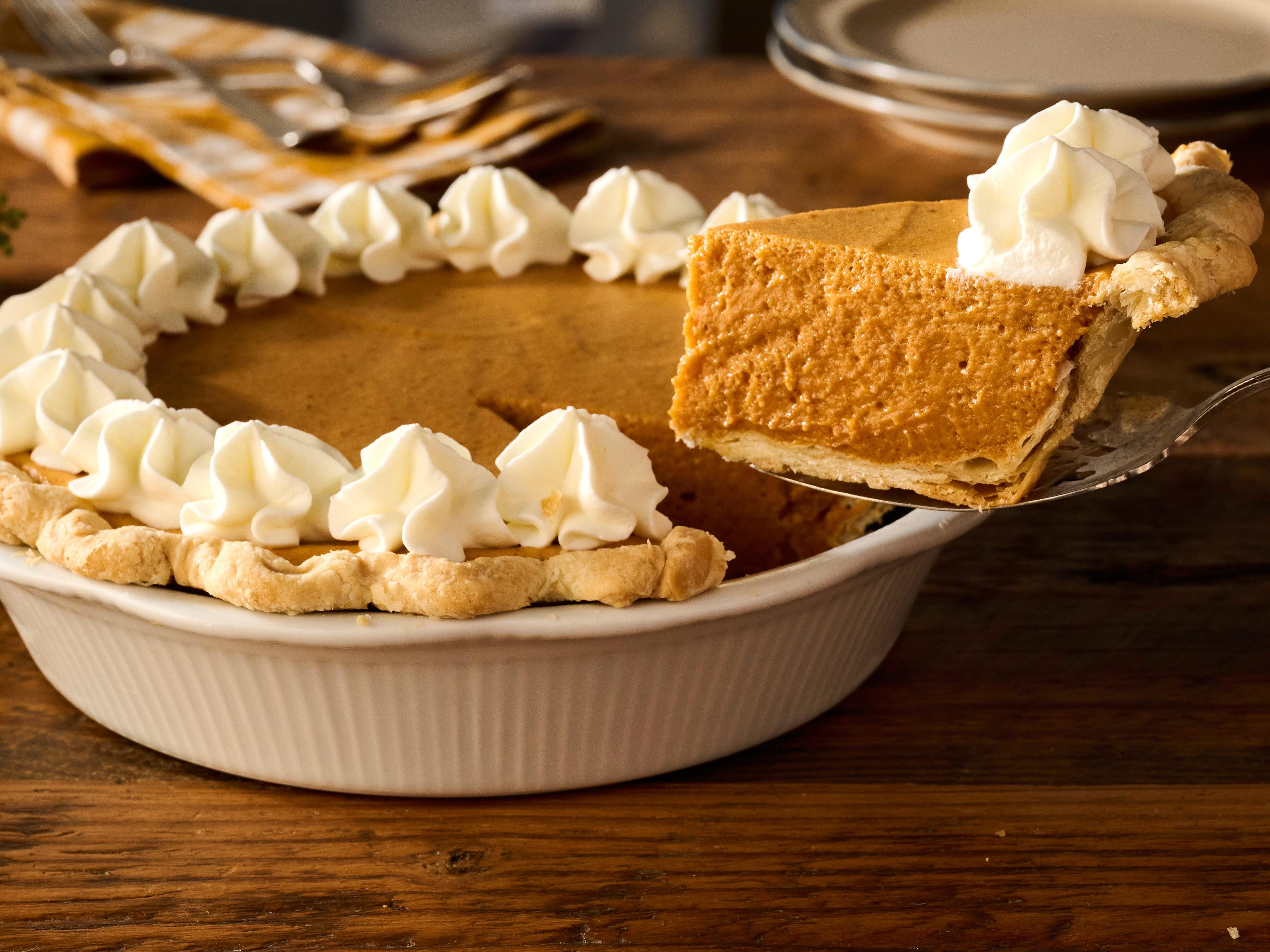 Close-up of a slice of pumpkin pie with a swirl of whipped cream, garnished with a sprinkle of cinnamon