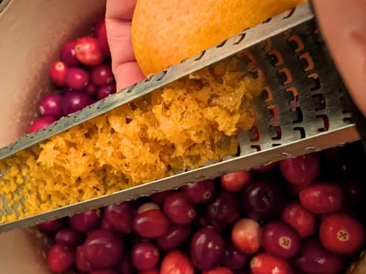 Hands zesting a fresh orange over a bowl of cranberries