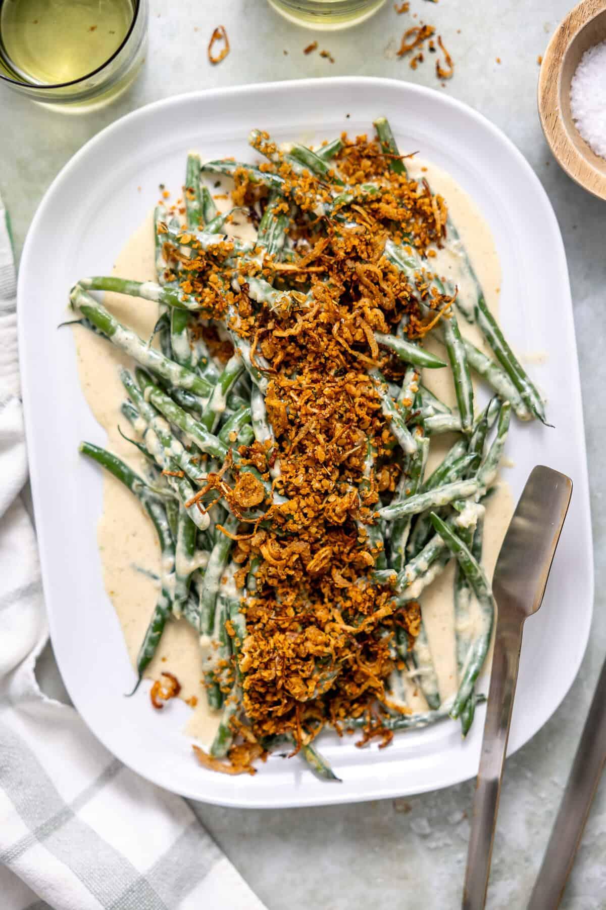 Hand serving a spoonful of Green Bean Parmesan Bake onto a plate, showing the creamy texture and golden topping.