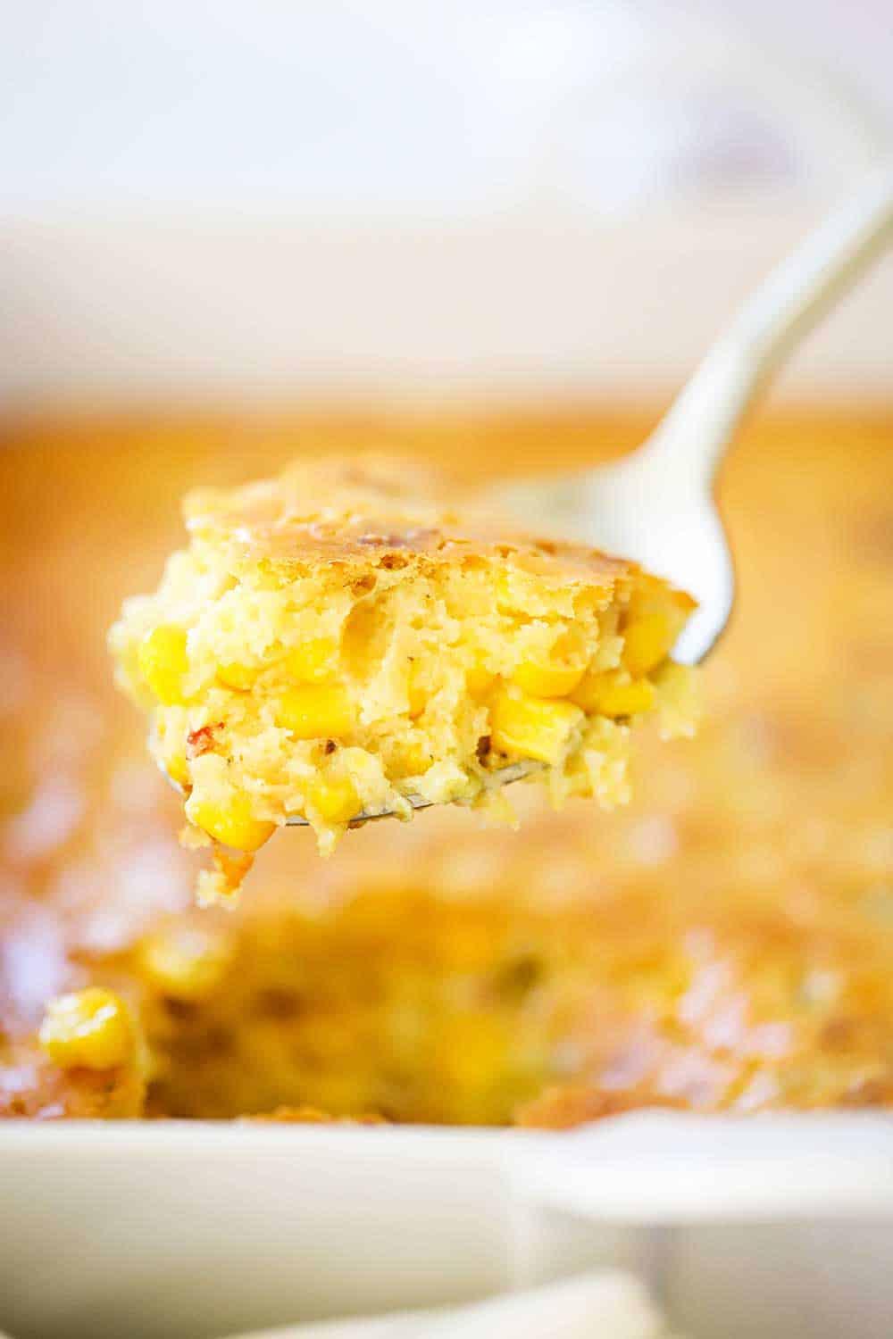 Close-up of a spoonful of corn casserole being lifted from the dish, showing the creamy interior and crispy top