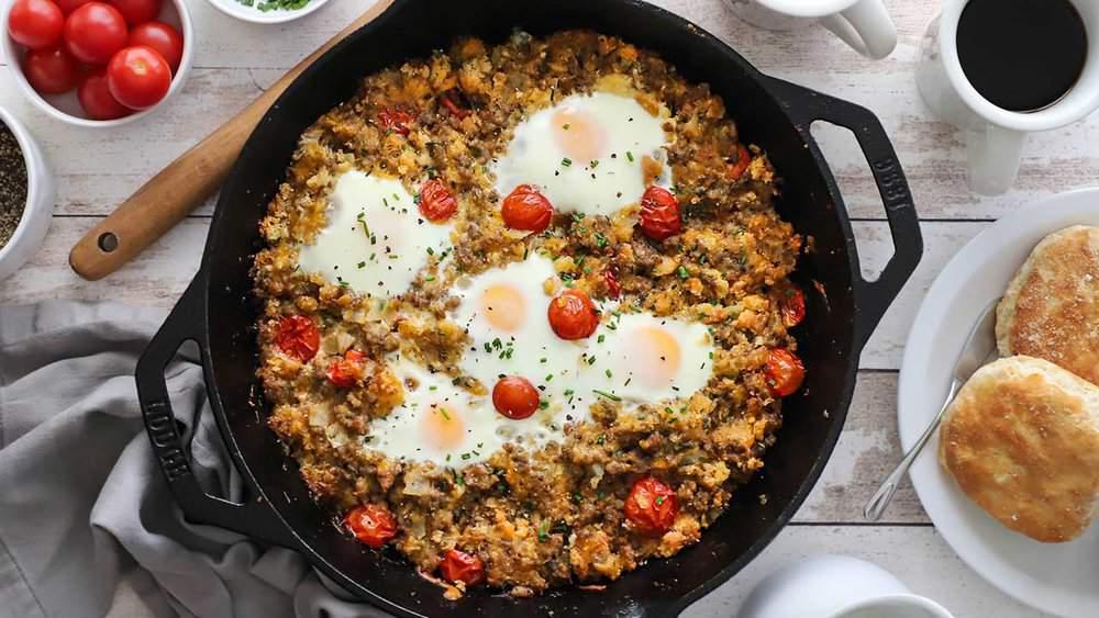 Sunny breakfast table with a cast iron skillet of tomato eggs, cup of coffee, and fresh basil
