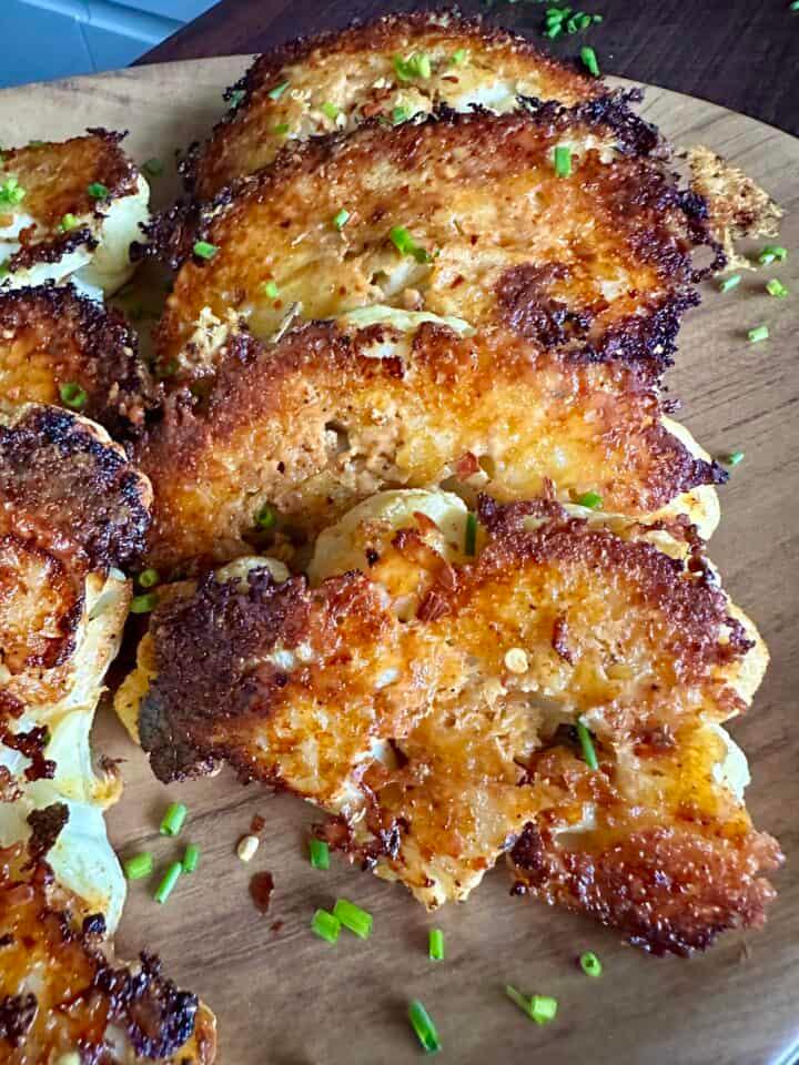 a baking sheet filled with garlic herb cauliflower steaks with parmesan crumble baking in the oven