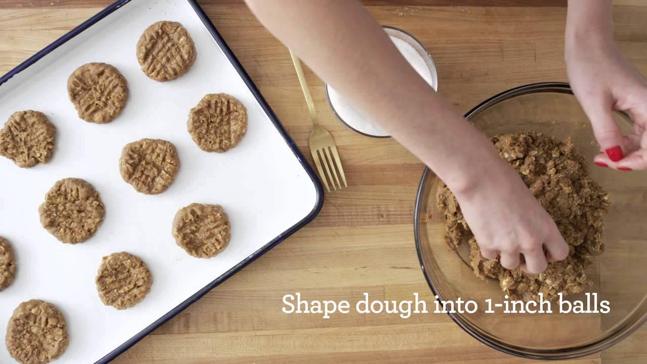 overhead shot of hands making crisscross pattern on raw peanut butter cookie dough on a baking sheet