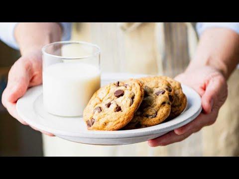 Smiling person enjoying a piece of triple-chip cookie slab with a glass of milk