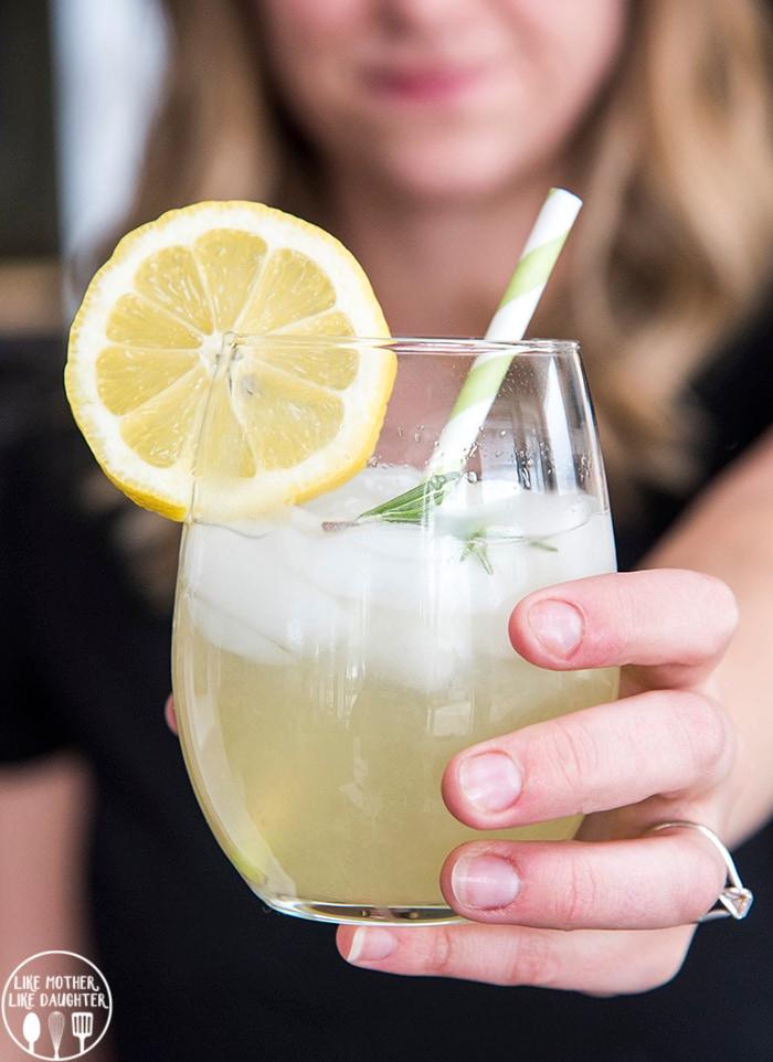 hands pouring rosemary lemonade into a glass with ice