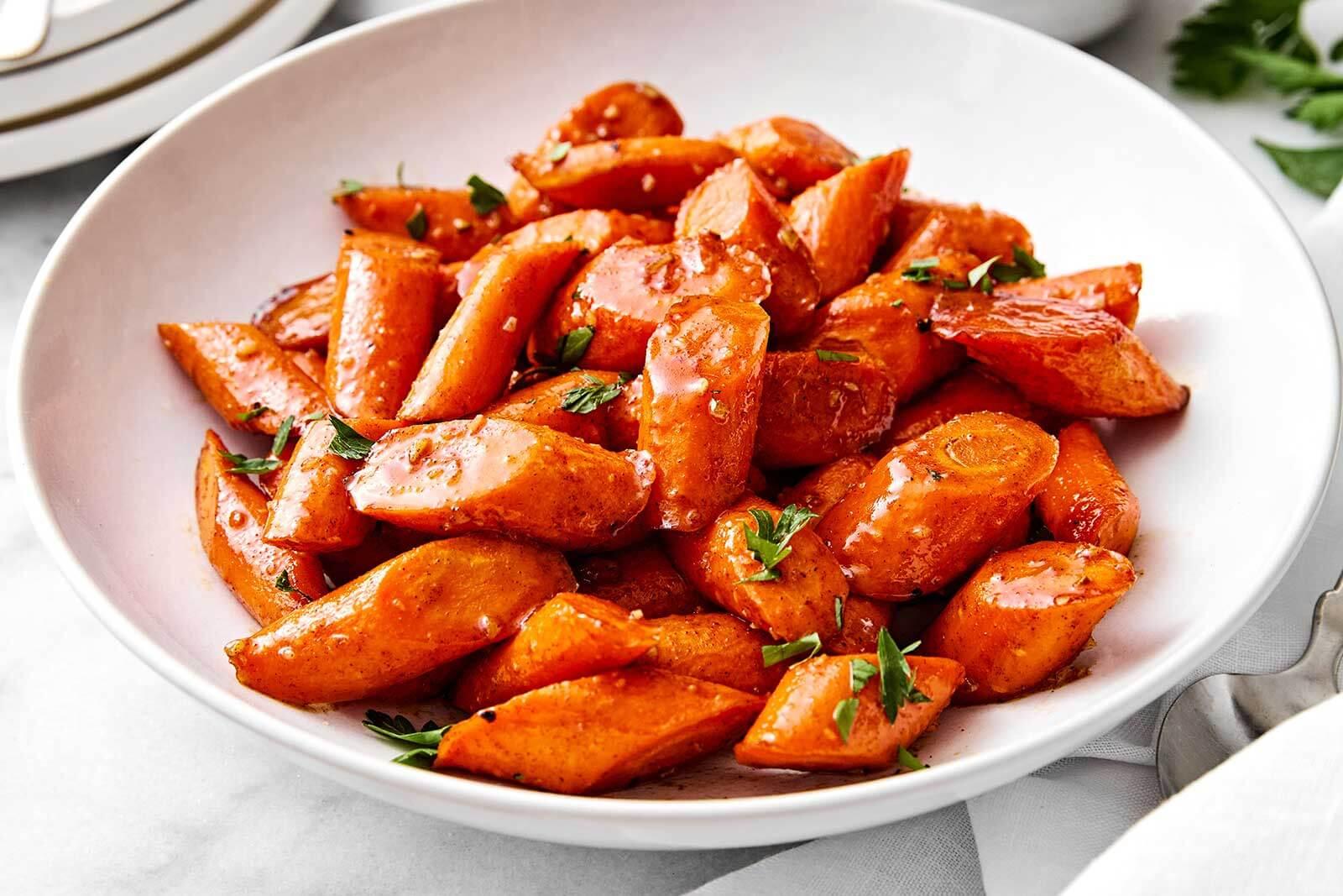 Vibrant honey glazed carrots in a serving dish, soft focus background