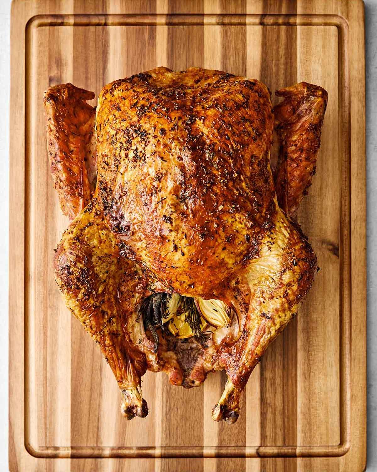 Thick slice of juicy roasted turkey breast on a carving board with vibrant fresh herbs and a drizzle of pan juices