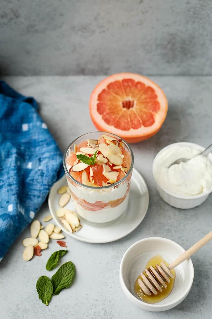 close up of a glass layering yogurt, grapefruit segments, and goji berries