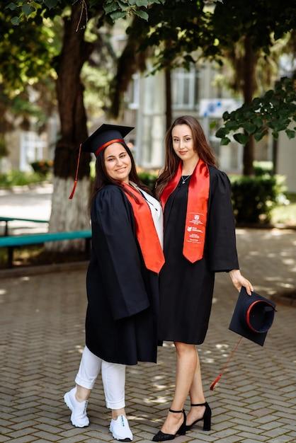 Two women in graduation dresses, one empire waist, one A-line, smiling and posing