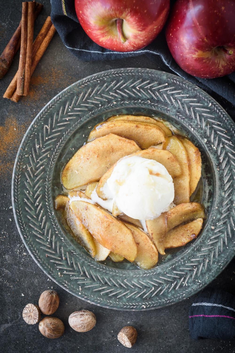 Hands mixing apple slices with cinnamon and sugar in a large bowl