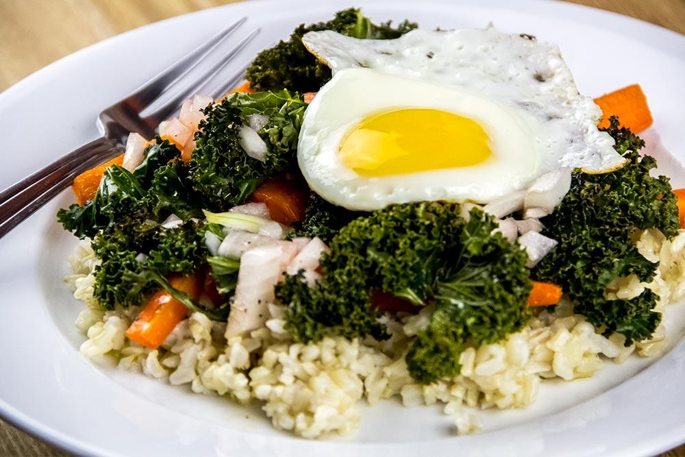 a perfectly cooked egg on top of a brown rice bowl with colorful veggies