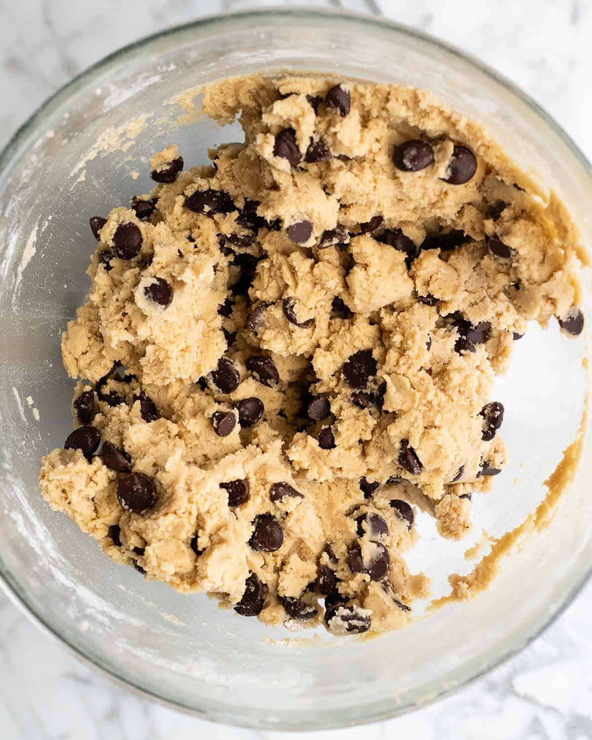 overhead shot of chocolate chip cookie dough in a mixing bowl with chocolate chips, ready to be scooped